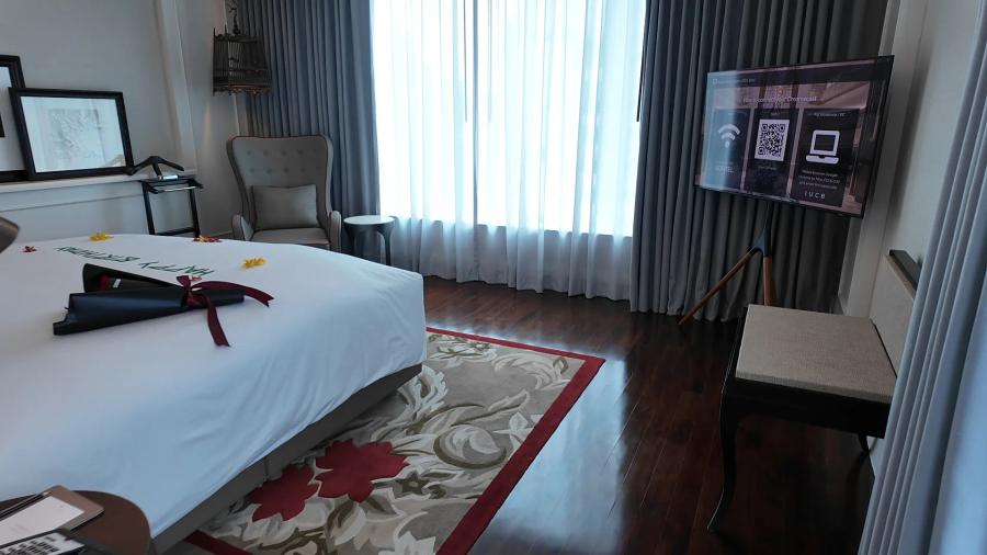 A king bed at Sofitel Bangkok Sukhumvit with Happy Birthday spelled out in flower petals and a ribbon bow, an armchair and sheer curtains behind.