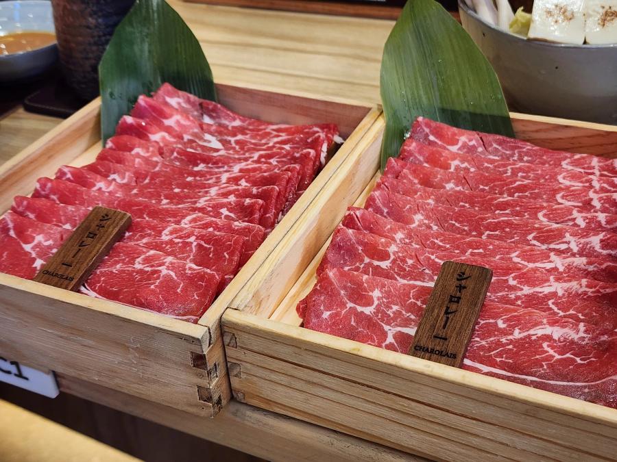 Two wooden boxes of thinly sliced marbled Charolais beef on bamboo leaves, each with a dark wooden tag reading Charolais in Japanese and English.