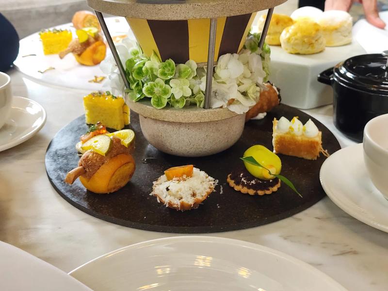 Small sweets arranged on a dark round board around a bowl of green and white hydrangea, with scones and a black cast iron pot behind.