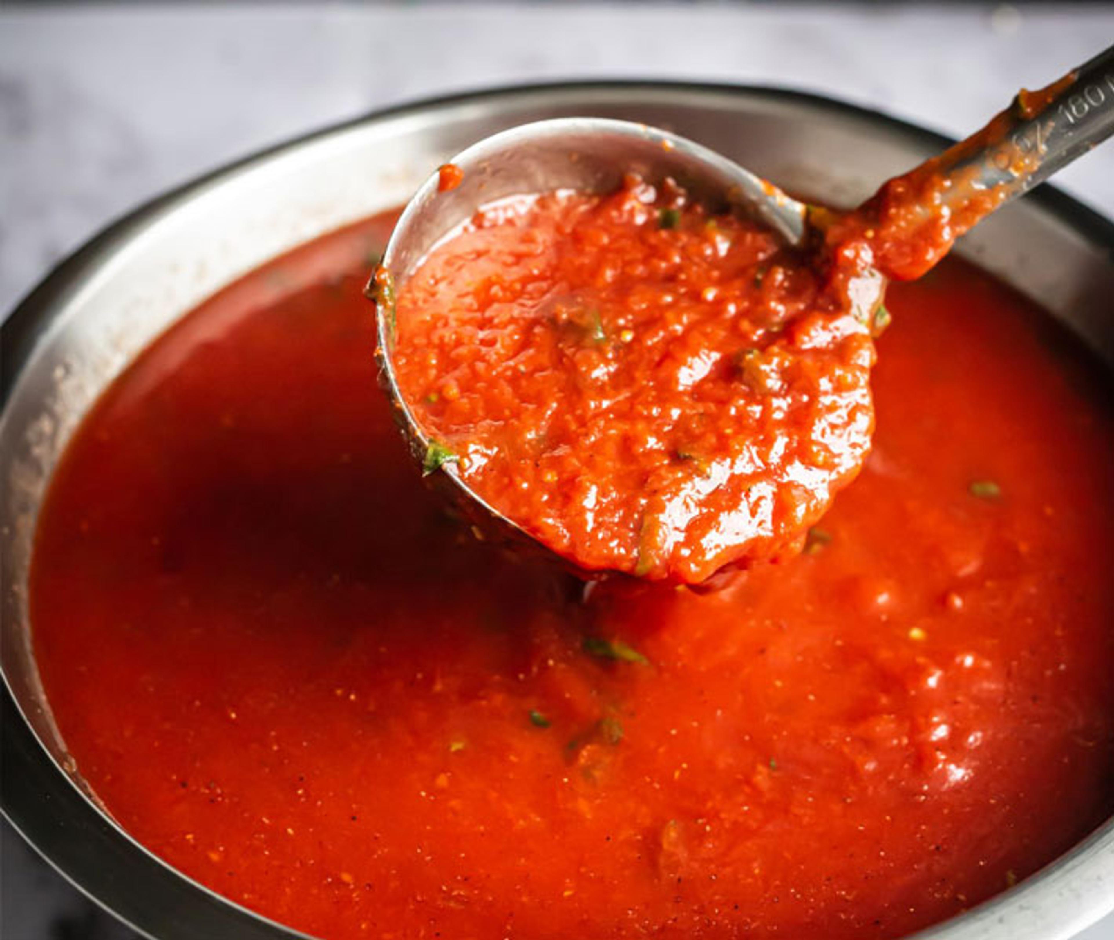 Ladle lifting fresh tomato sauce from a pot