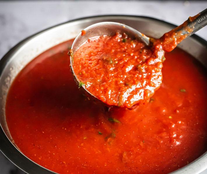 Ladle lifting fresh tomato sauce from a pot