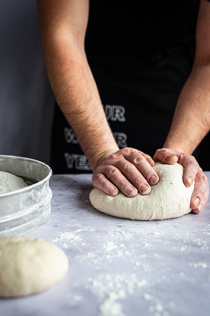 Hands kneading pizza dough on a marble counter