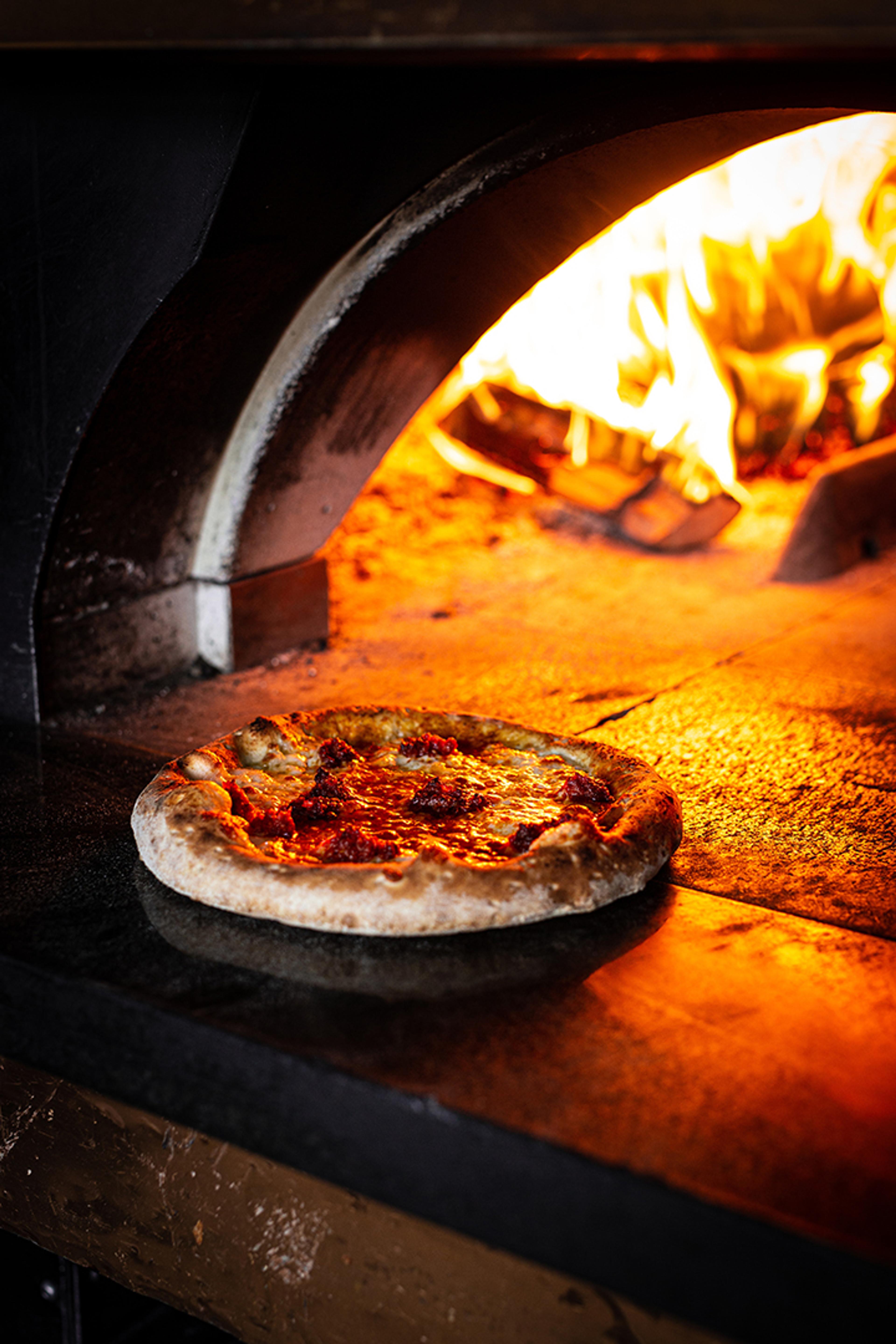 Pizza baking in a wood fired oven with flames behind it