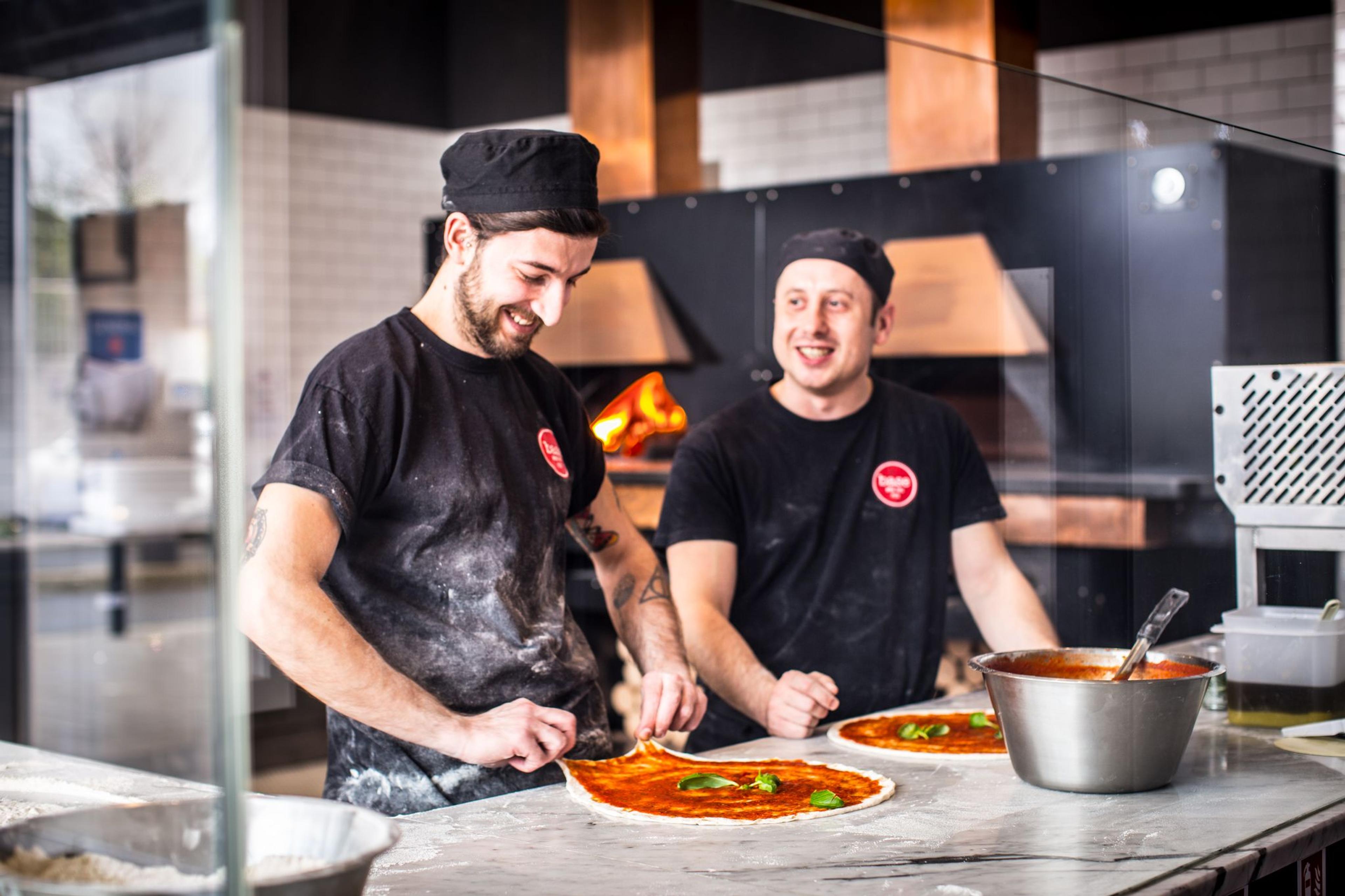 Two Base chefs topping pizzas in the kitchen