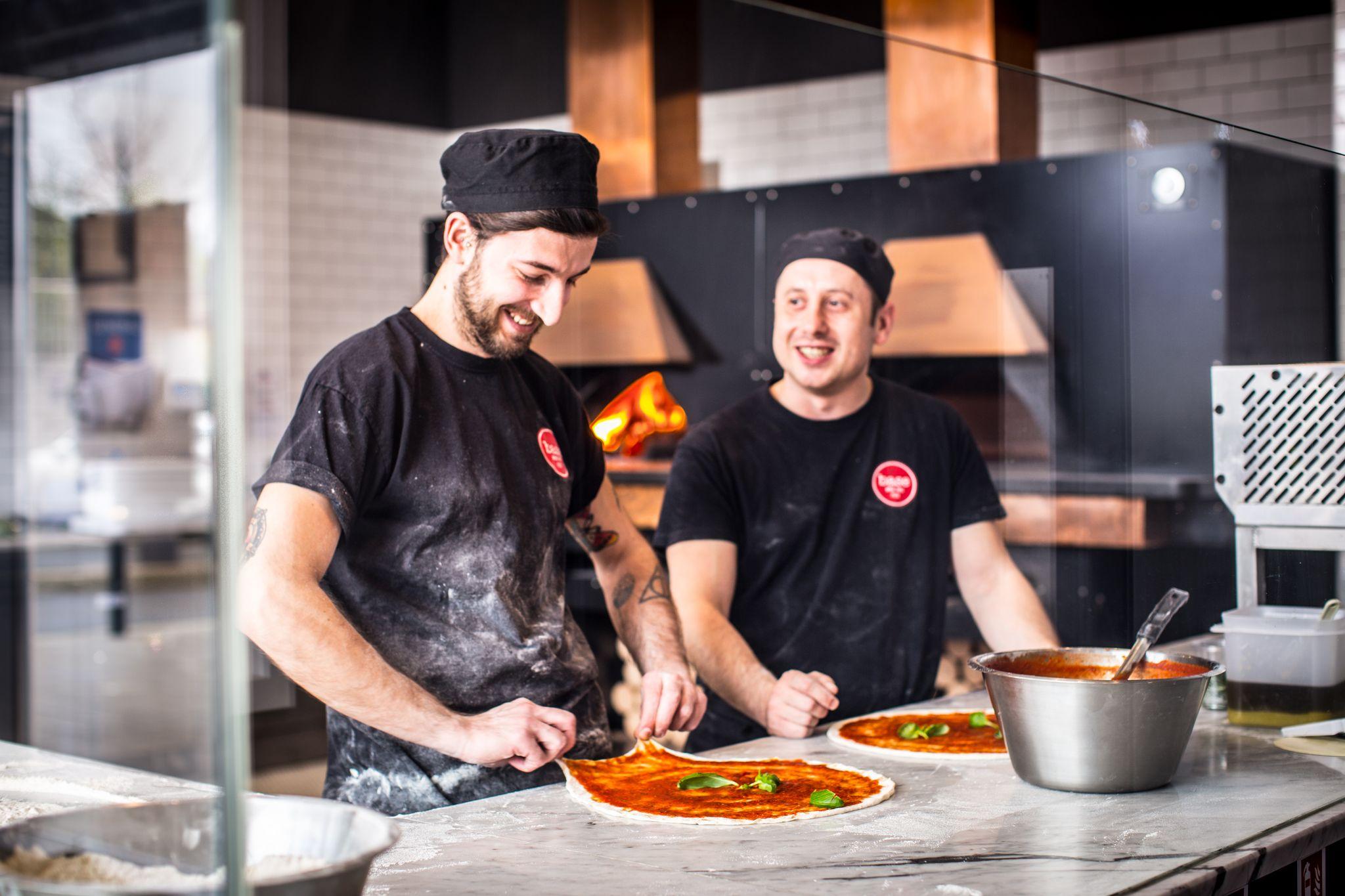Two Base chefs topping pizzas in the kitchen