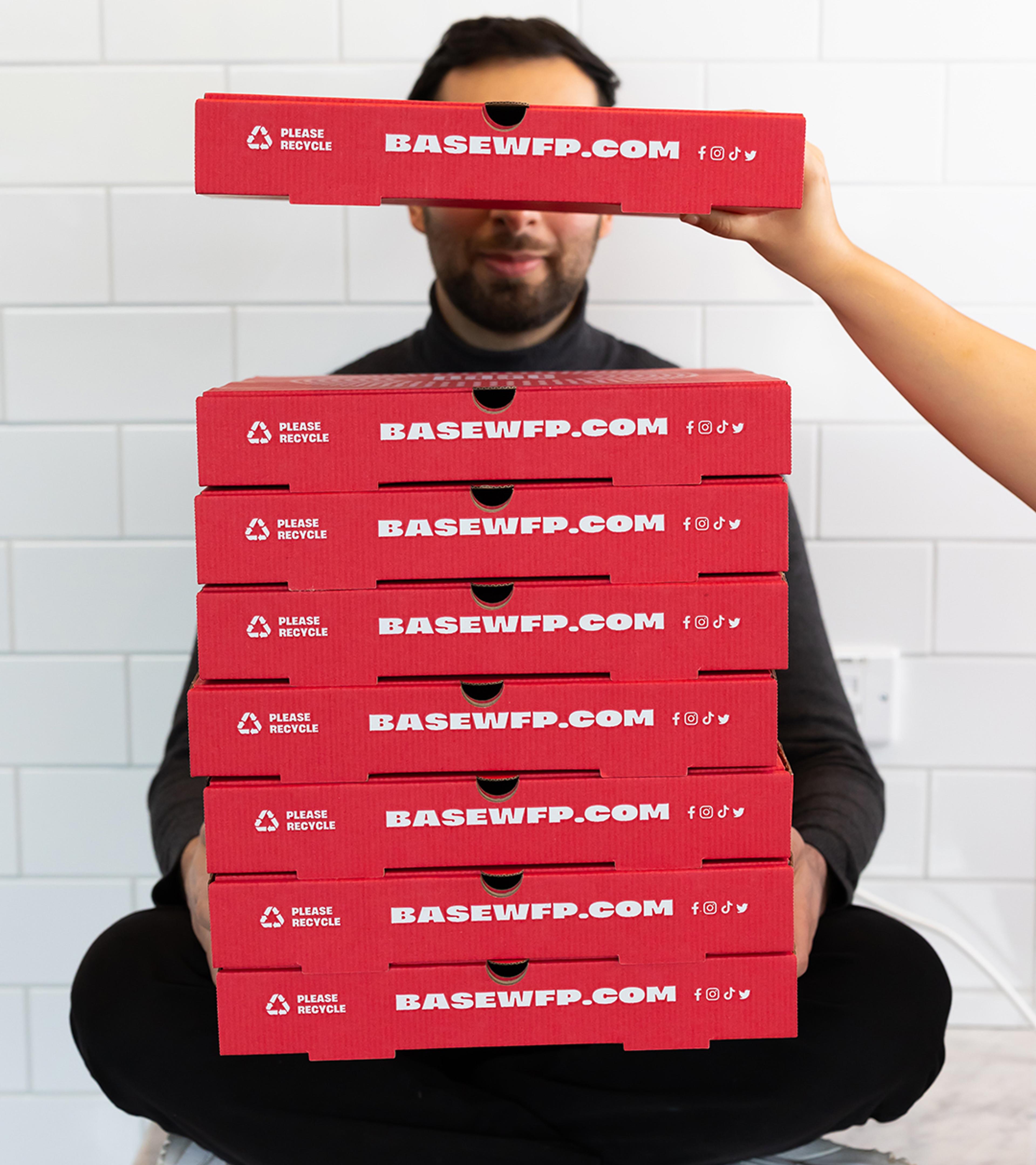 Person sitting on the floor holding a tall stack of red Base pizza boxes