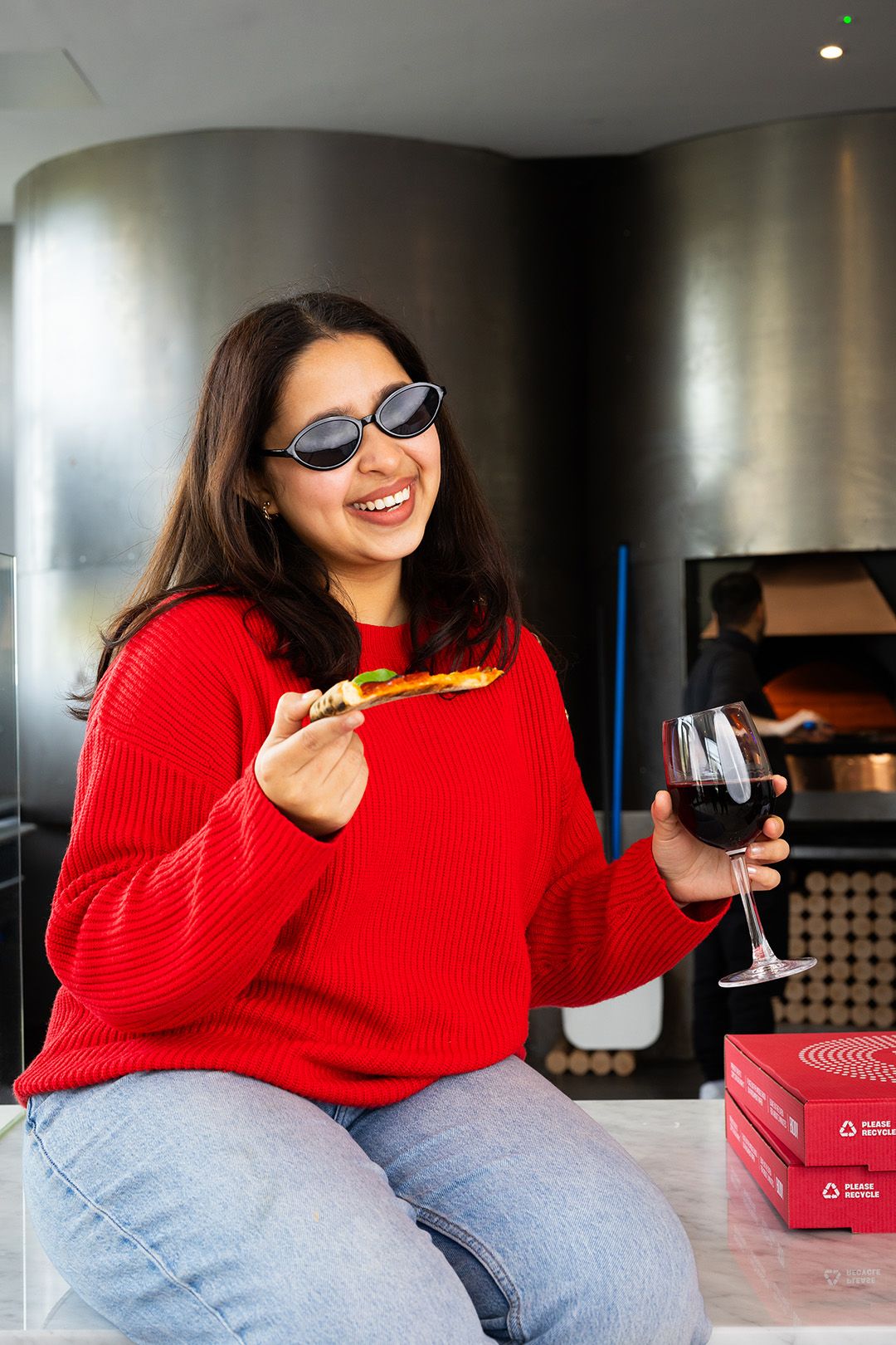Woman in sunglasses enjoying a slice of pizza and a glass of wine