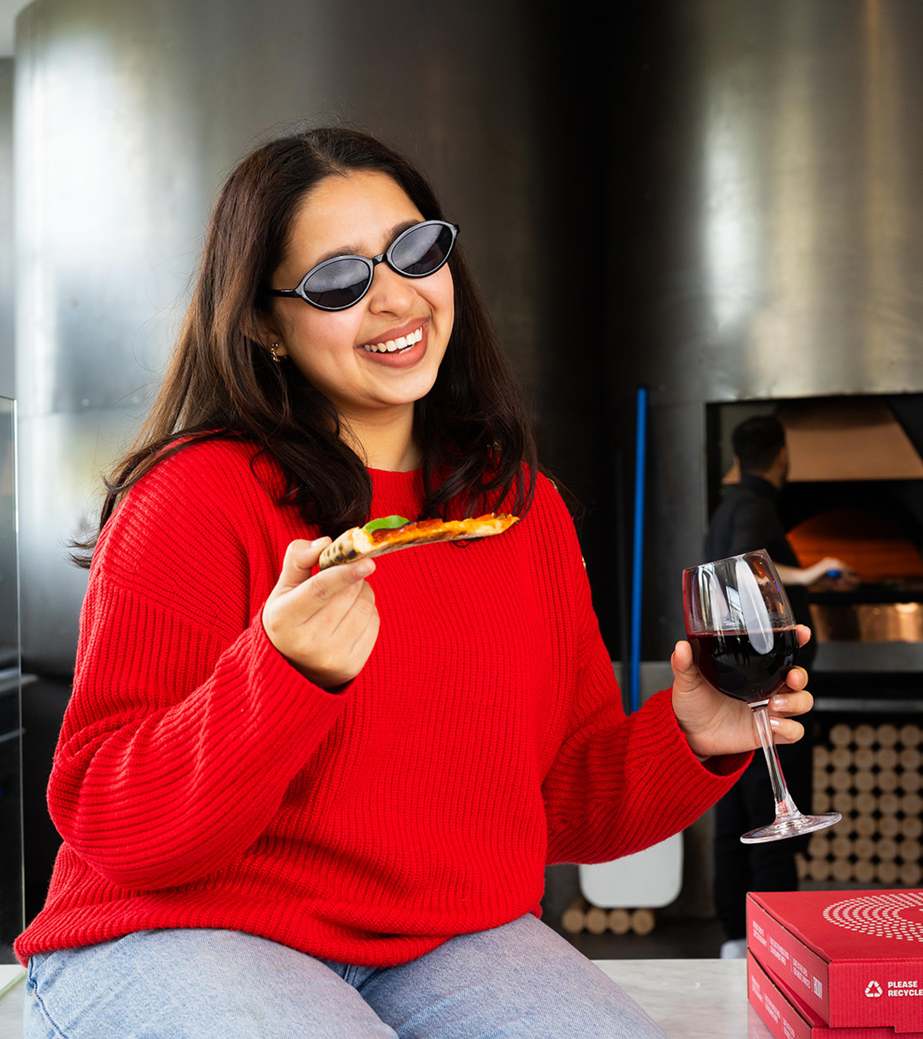Woman in sunglasses enjoying a slice of pizza and a glass of wine