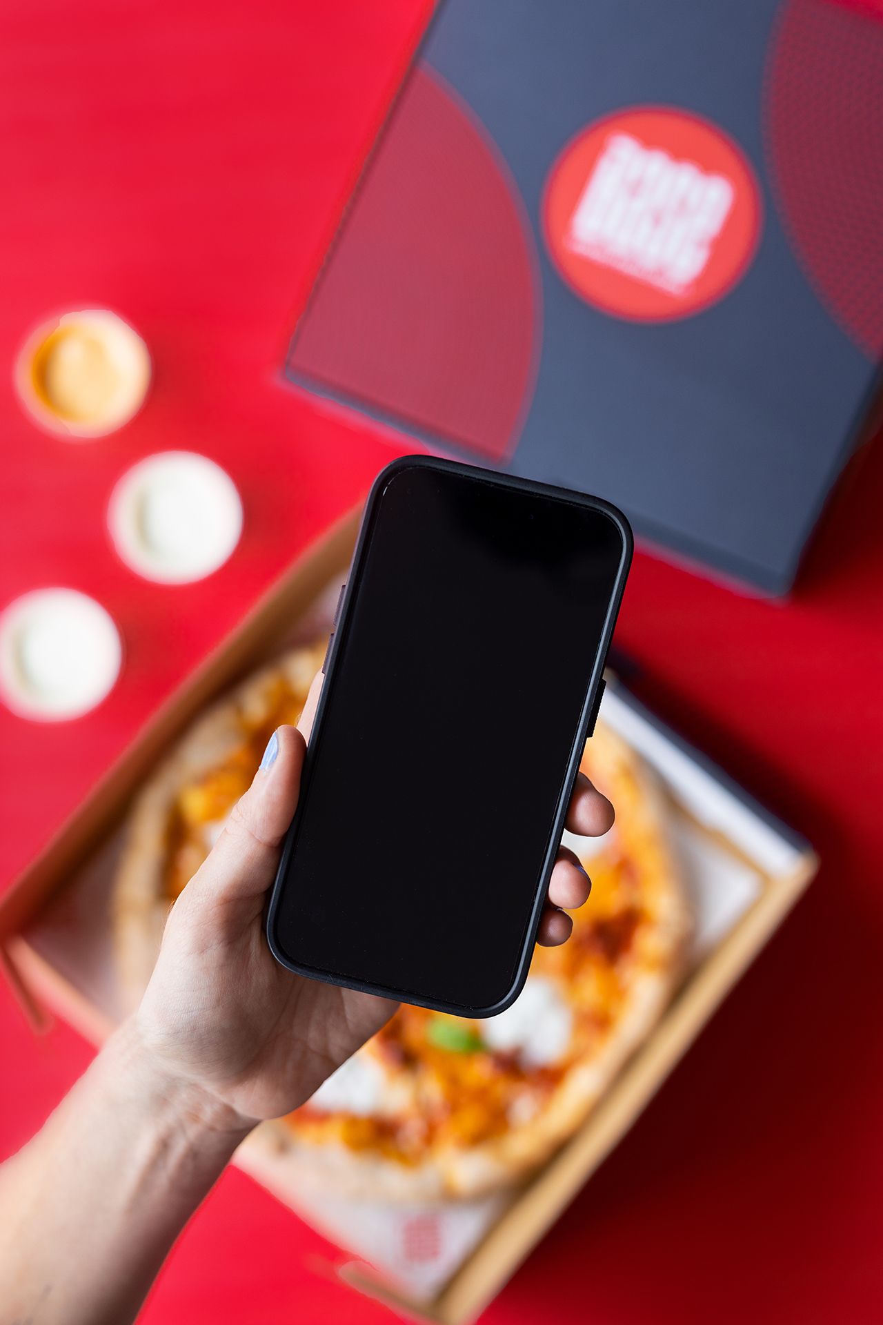 Hand holding a phone above an open Base pizza box