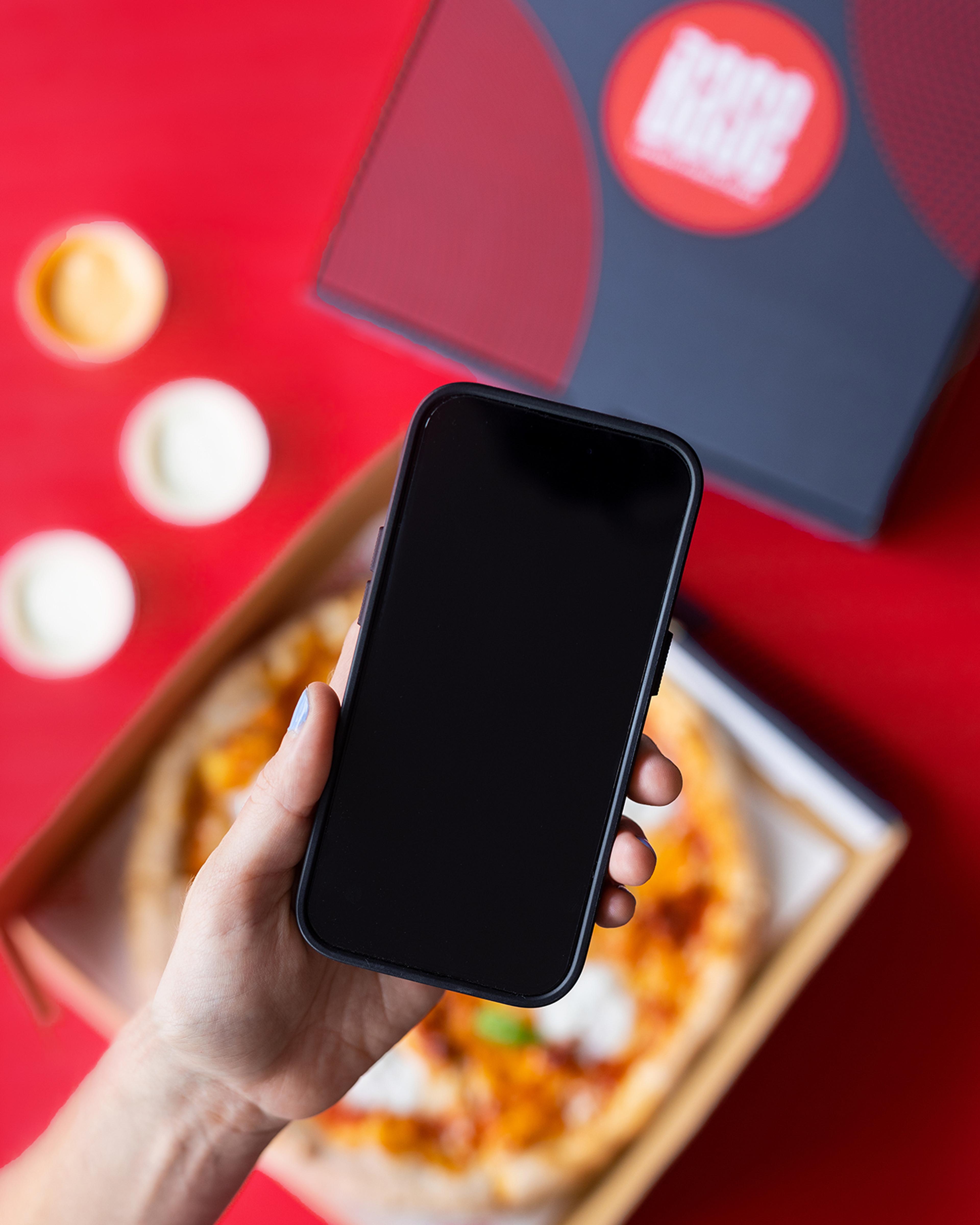 Hand holding a phone above an open Base pizza box