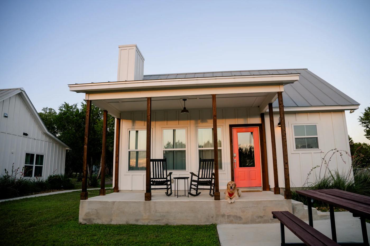 A farmhouse cottage at Wayside Wimberley at dusk, with a golden retriever resting on the front porch