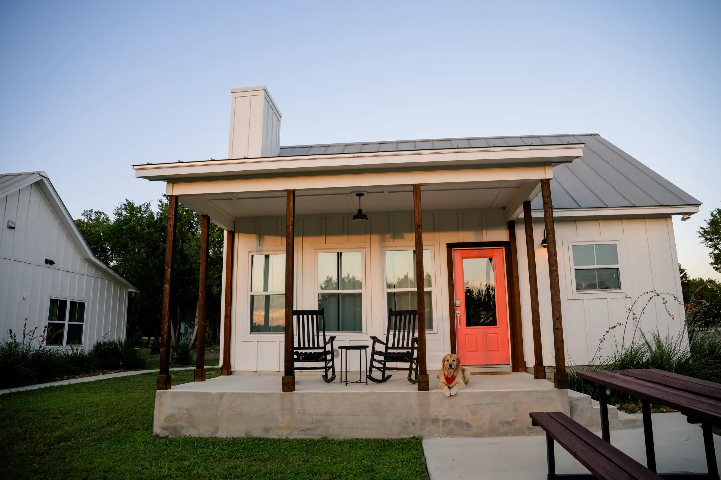 A farmhouse cottage at Wayside Wimberley at dusk, with a golden retriever resting on the front porch