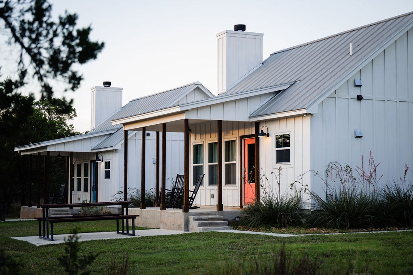 Both farmhouse cottages at Wayside Wimberley — Summermoon with its pink door and Jackrabbit with its blue door — with covered porches and rocking chairs