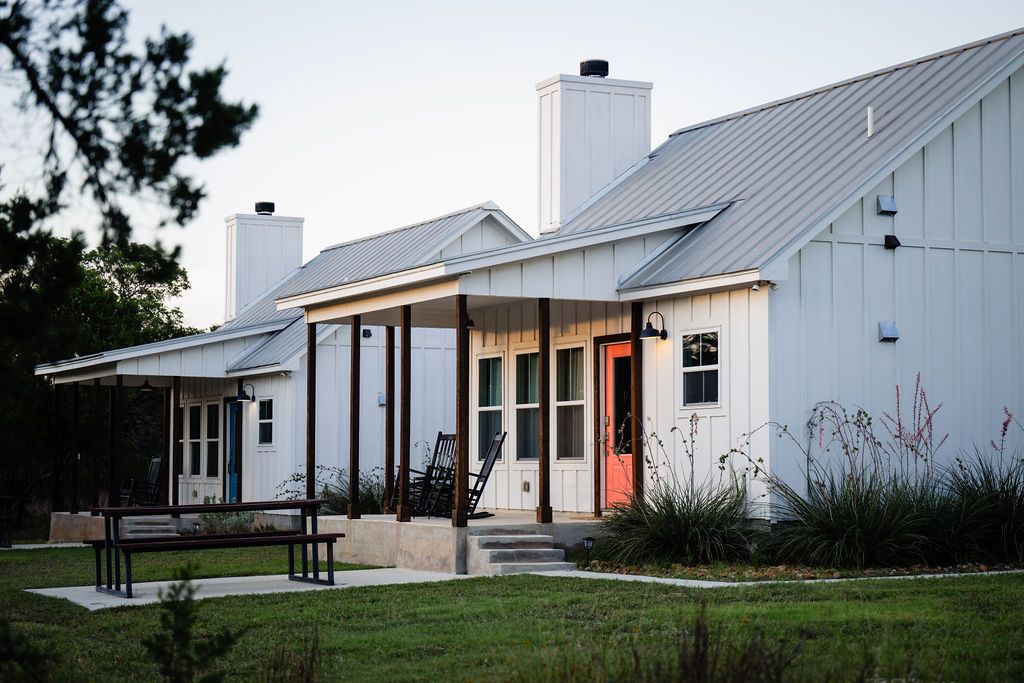 Both farmhouse cottages at Wayside Wimberley — Summermoon with its pink door and Jackrabbit with its blue door — with covered porches and rocking chairs