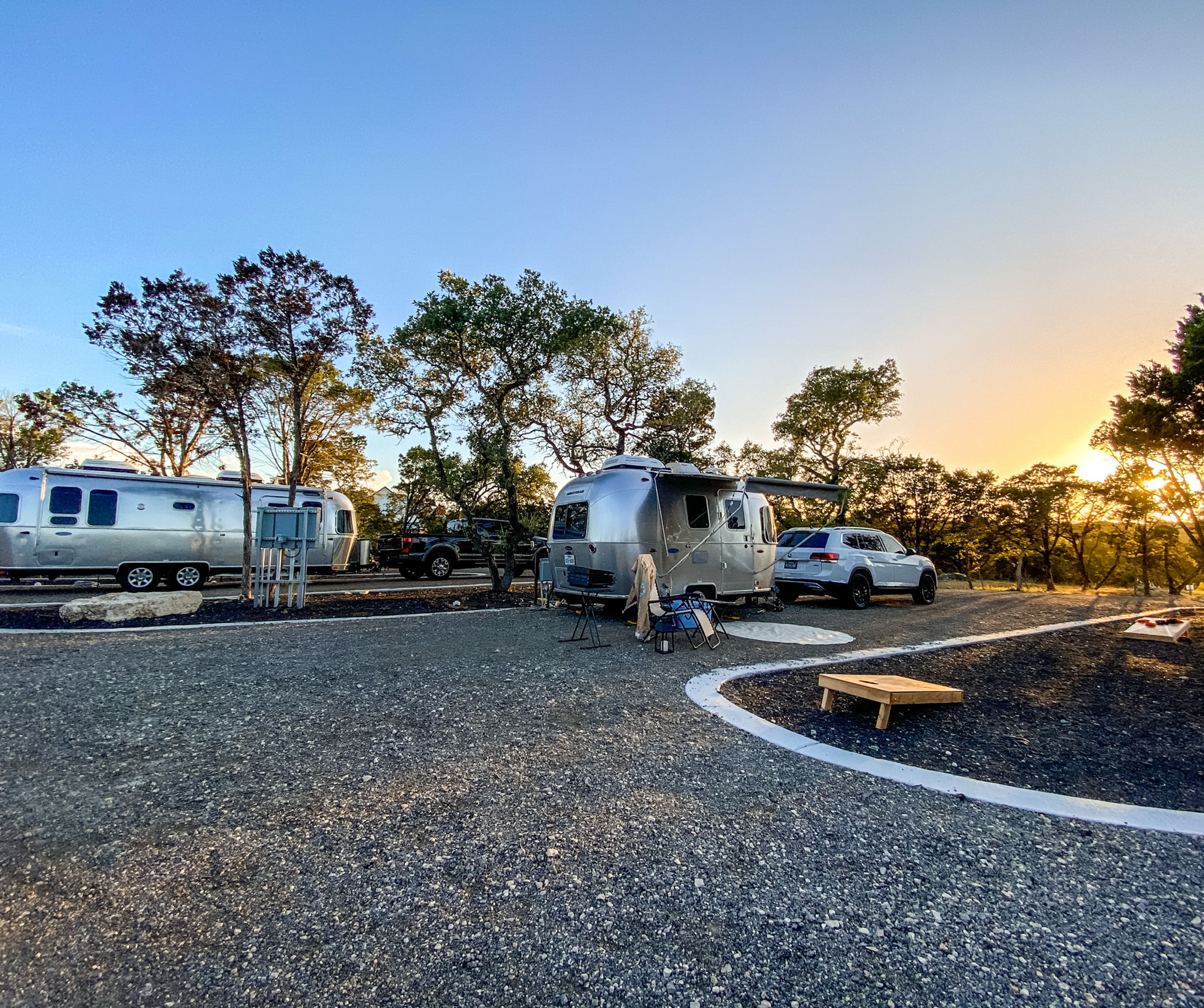 Airstream trailers parked on the pull-through RV sites at Wayside Wimberley with the sun setting through the oaks