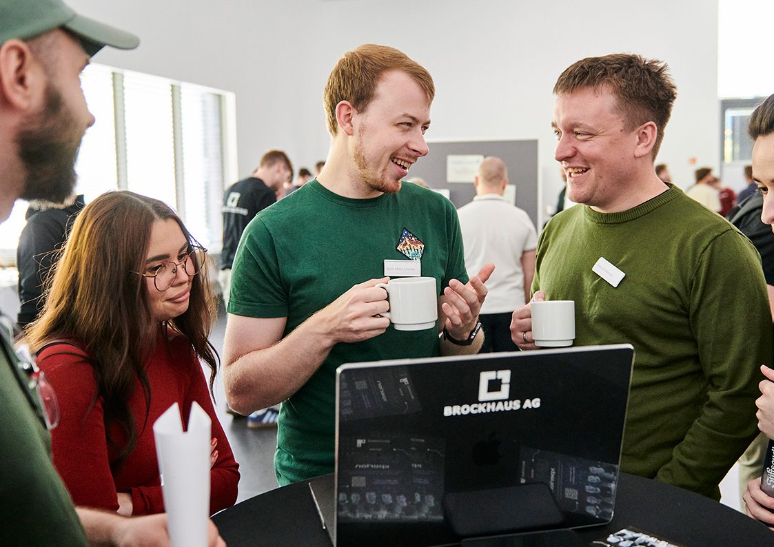 Mehrere Personen im fachlichen Austausch an einem Laptop als Symbol für Teamarbeit, Mentoring und Praxiserfahrung im Werkstudierendenjob bei BROCKHAUS