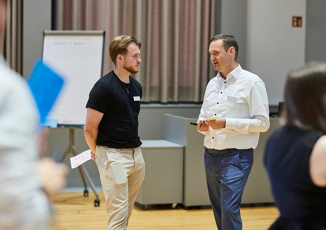 Dual Studierender im fachlichen Austausch mit einem erfahrenen Mitarbeitenden über ein Praxisprojekt in der Softwareentwicklung