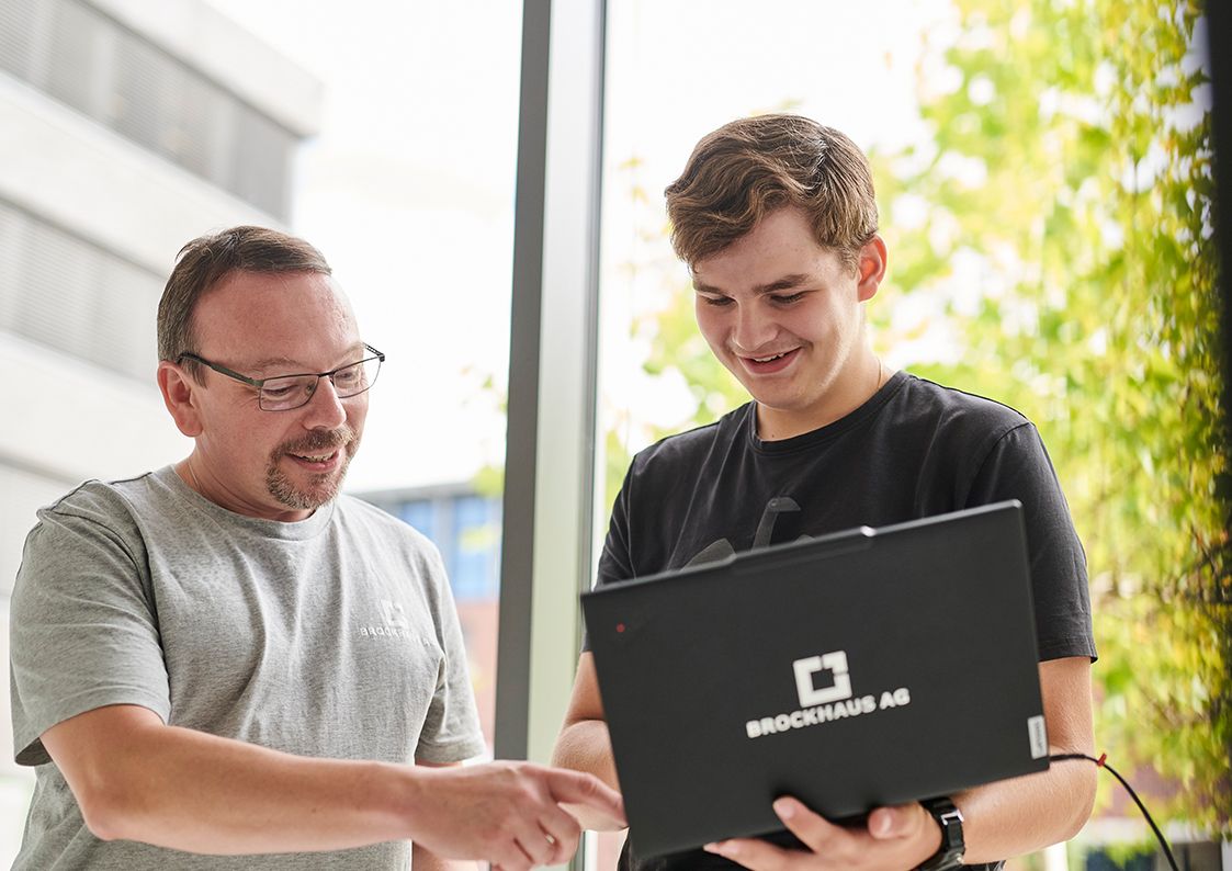 Auszubildendes IT-Talent erhält Unterstützung bei einem Softwareentwicklungsprojekt durch einen erfahrenen Kollegen der BROCKHAUS AG