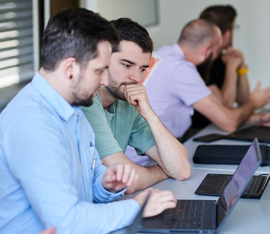 Mehrere Auszubildende und Mitarbeitende arbeiten mit Laptops in einer modernen Arbeitsumgebung zusammen.