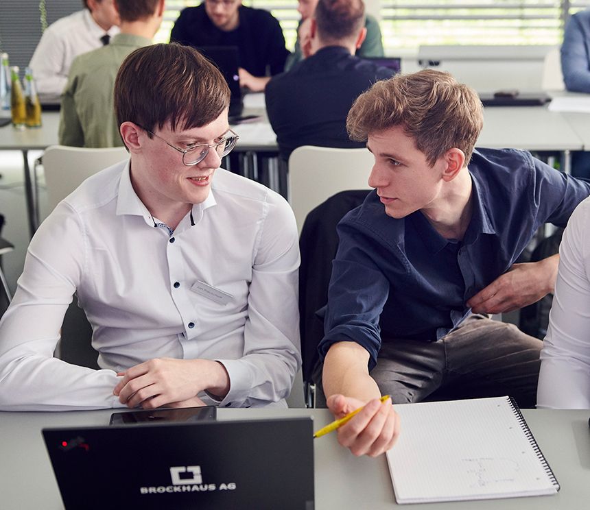 Praktikant erhält Unterstützung durch ein erfahrenes Crewmitglied bei einer Aufgabe aus der Softwareentwicklung