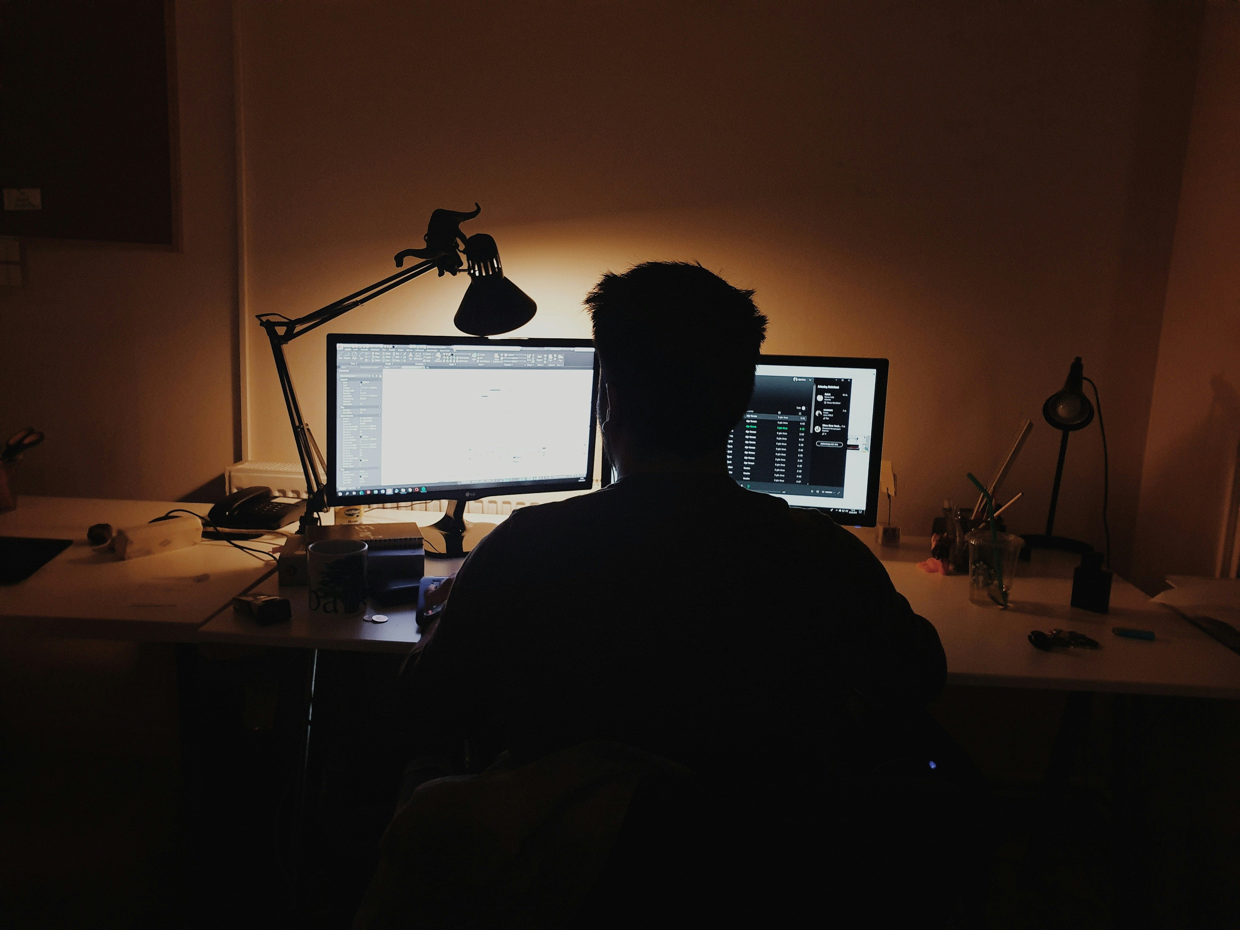 A professional working alone at a wooden desk at night with a laptop 