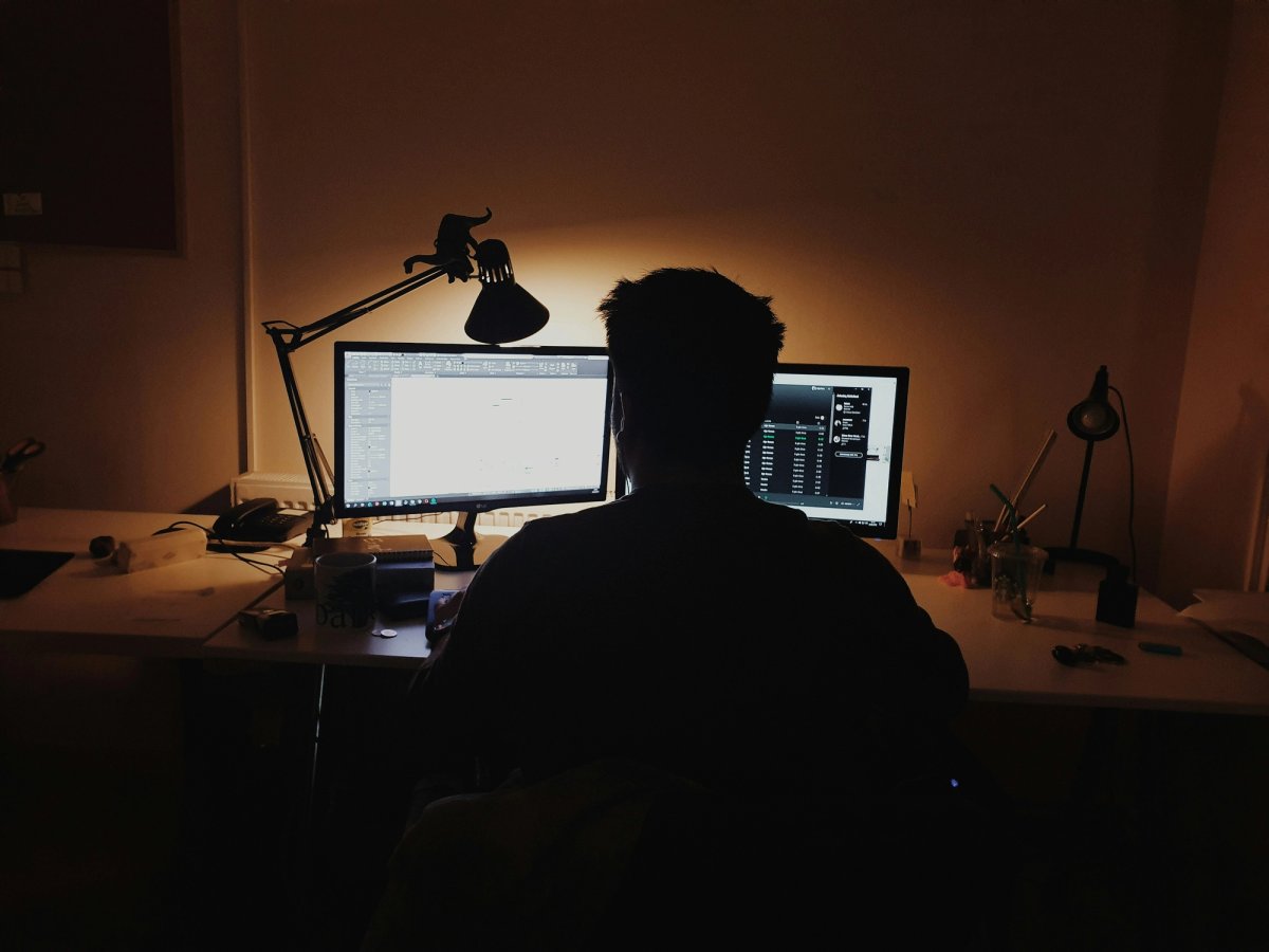 A professional working alone at a wooden desk at night with a laptop 