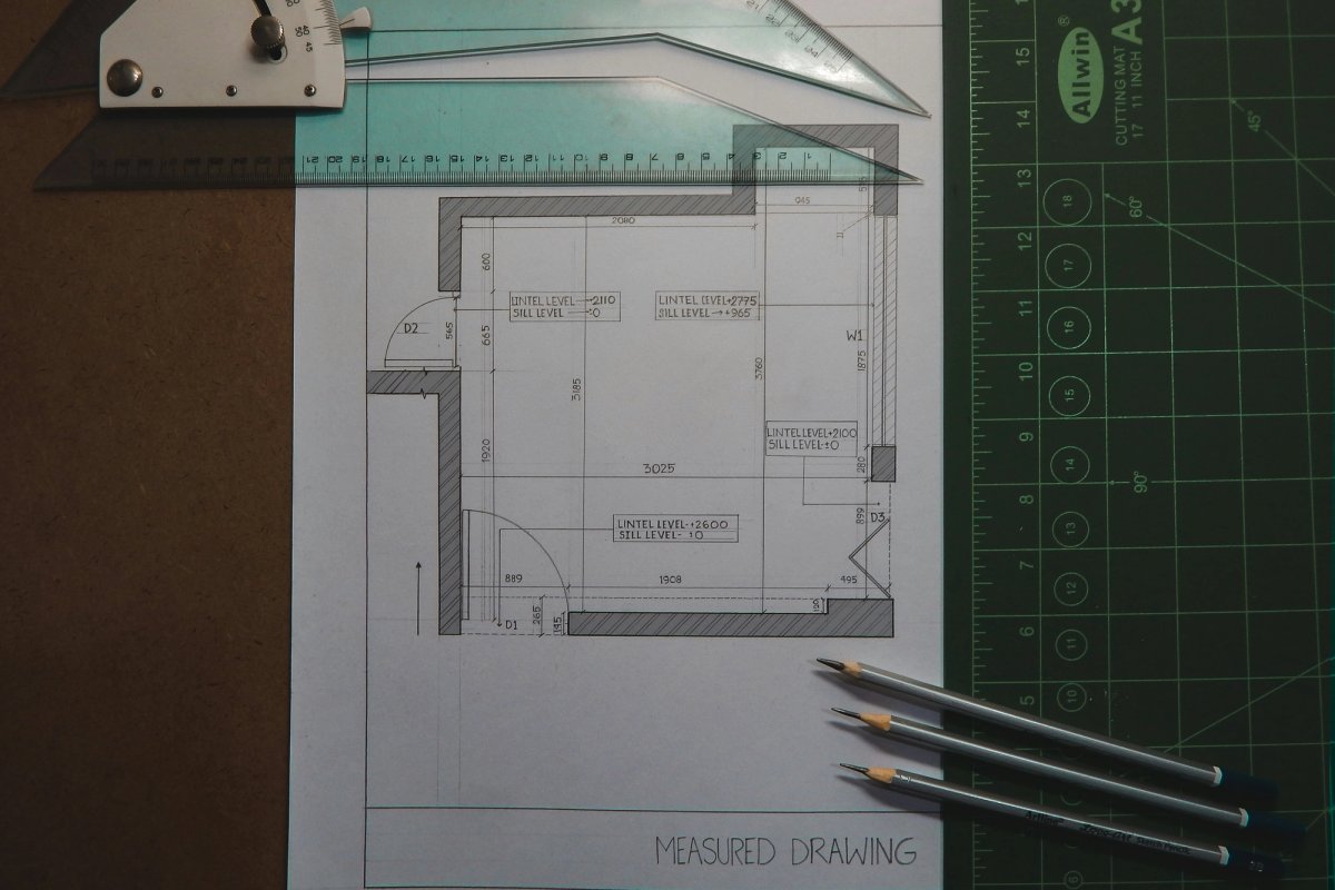 A measured architectural drawing on a desk with a set square, a cutting mat and three pencils