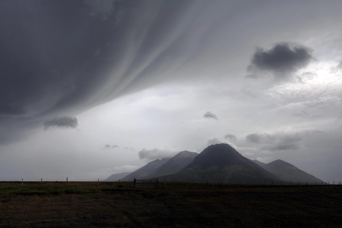 a cloudy sky over a mountain range with a fence in the foreground in iceland.