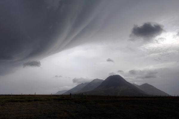 a cloudy sky over a mountain range with a fence in the foreground in iceland.