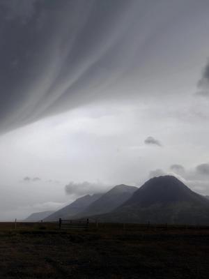 a cloudy sky over a mountain range with a fence in the foreground in iceland.