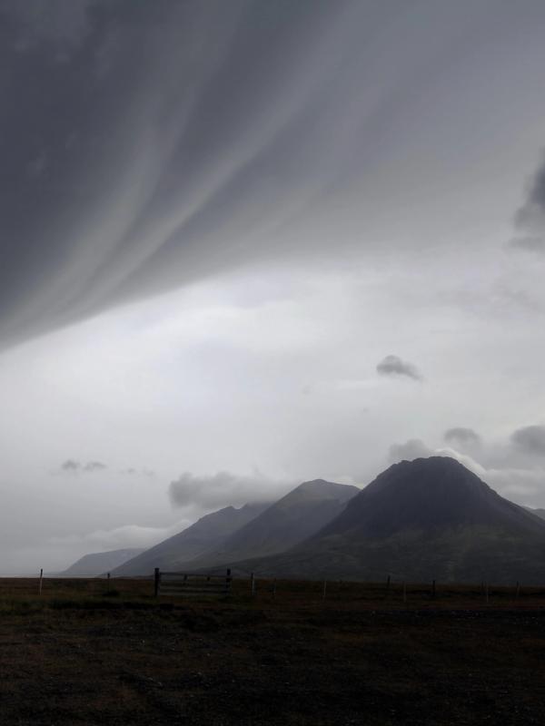 a cloudy sky over a mountain range with a fence in the foreground in iceland.
