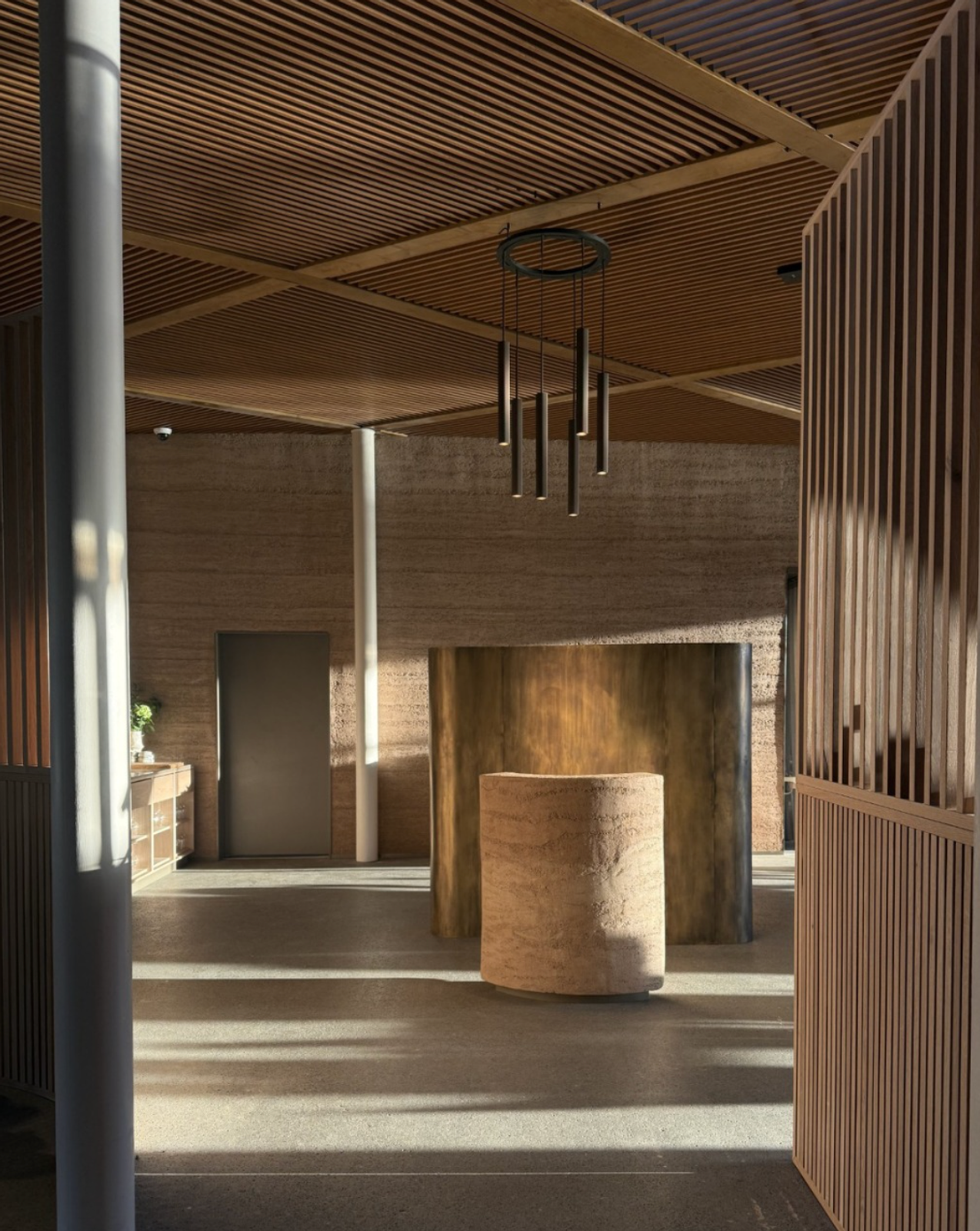 Interior moderno con muros de tierra apisonada, techo de listones de madera y un pedestal cilíndrico.