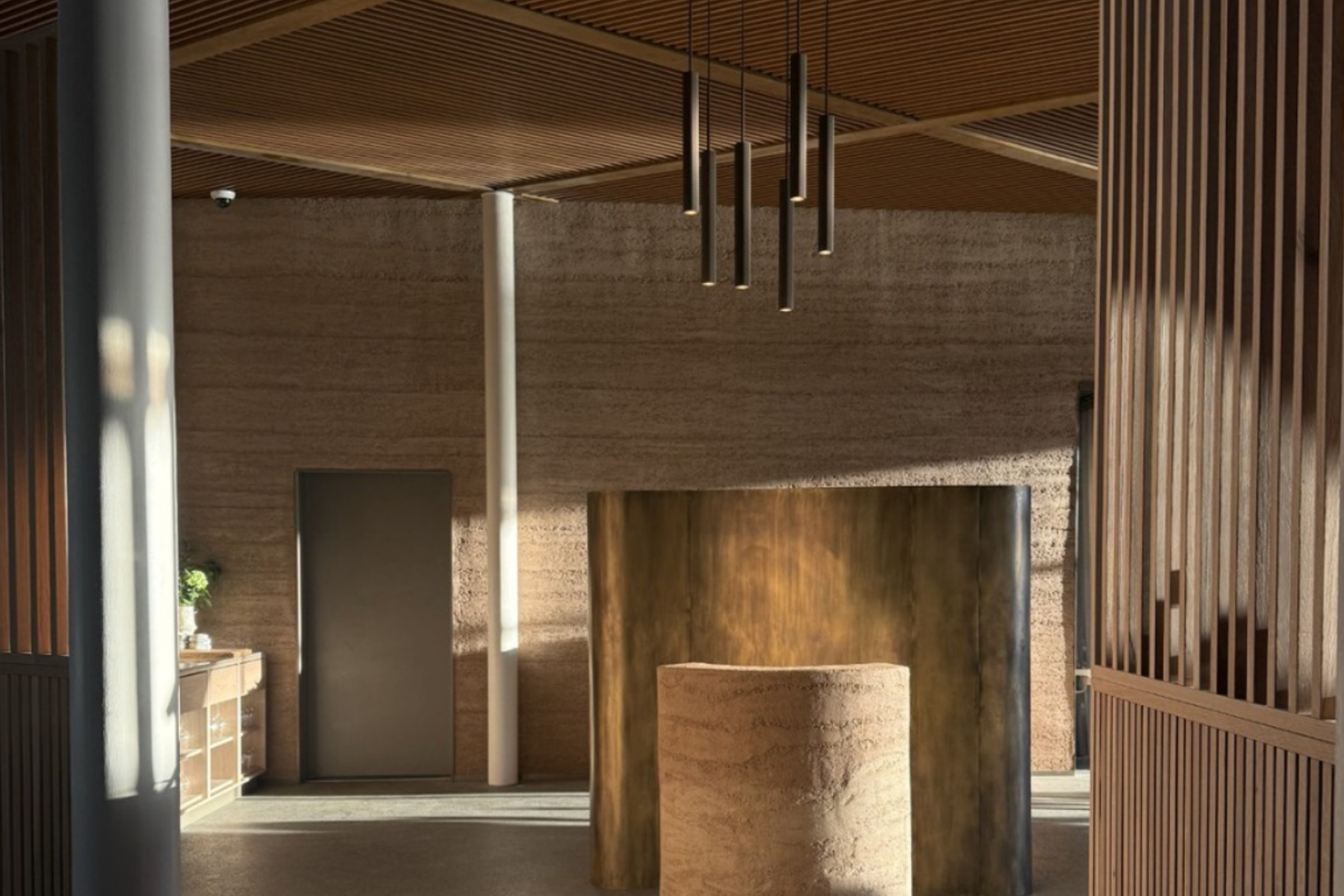 Interior moderno con muros de tierra apisonada, techo de listones de madera y un pedestal cilíndrico.