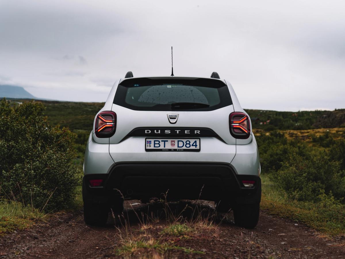 Vista trasera directa del Dacia Duster Vista trasera de un Dacia Duster estacionado en un camino de tierra, con matorrales a ambos lados