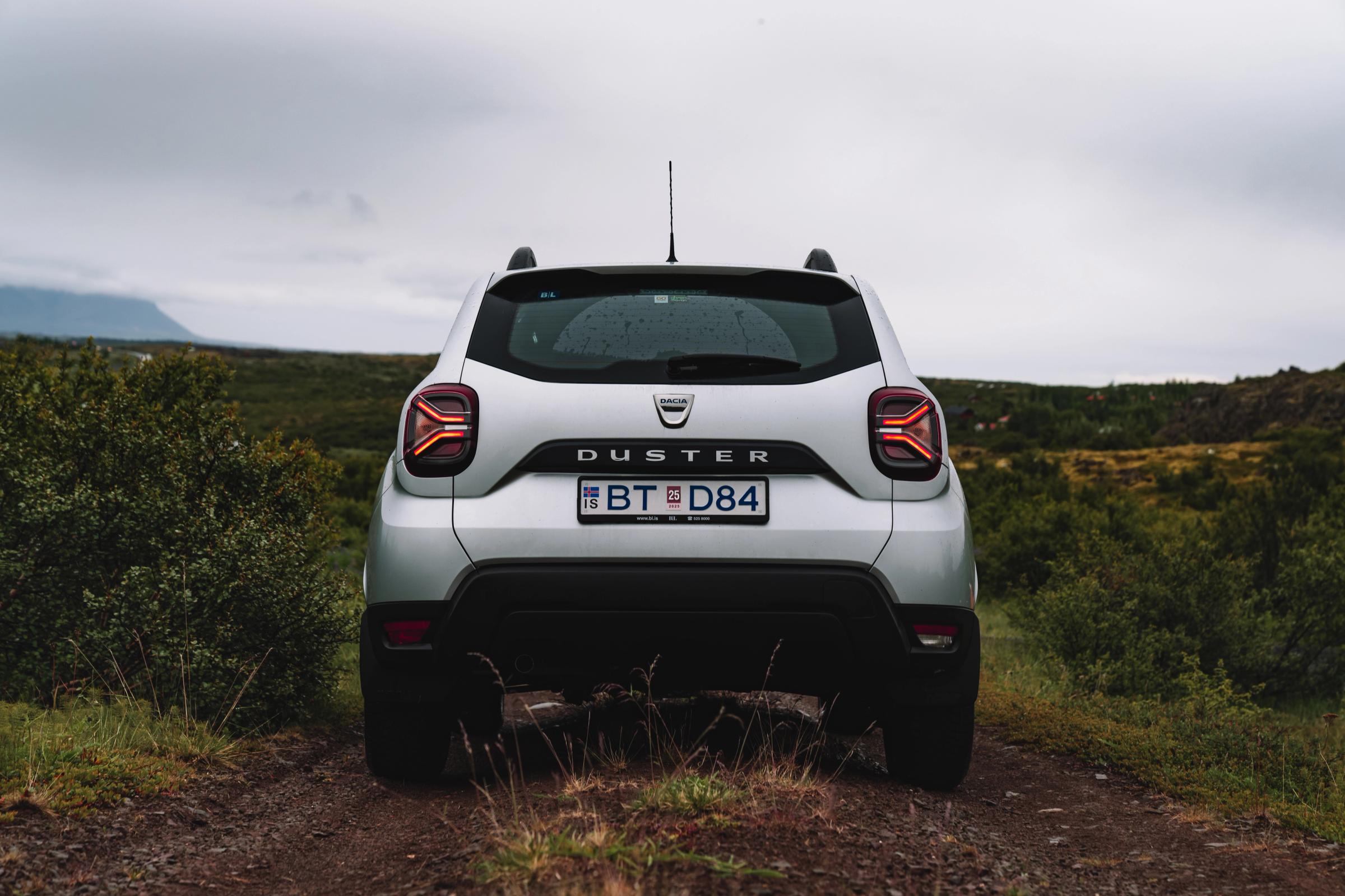 Vista trasera directa del Dacia Duster Vista trasera de un Dacia Duster estacionado en un camino de tierra, con matorrales a ambos lados