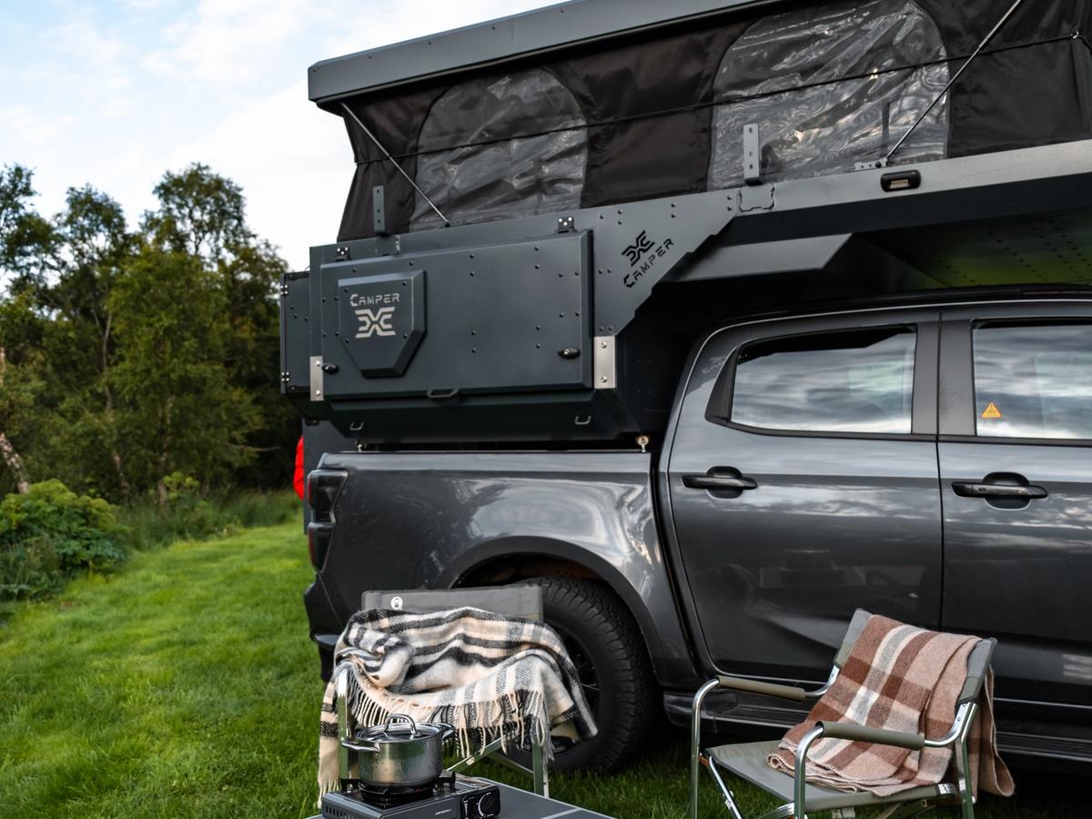 Mesa y hornillo de camping Mesa plegable con un hornillo portátil y una tetera junto a dos sillas bajo el techo elevable abierto