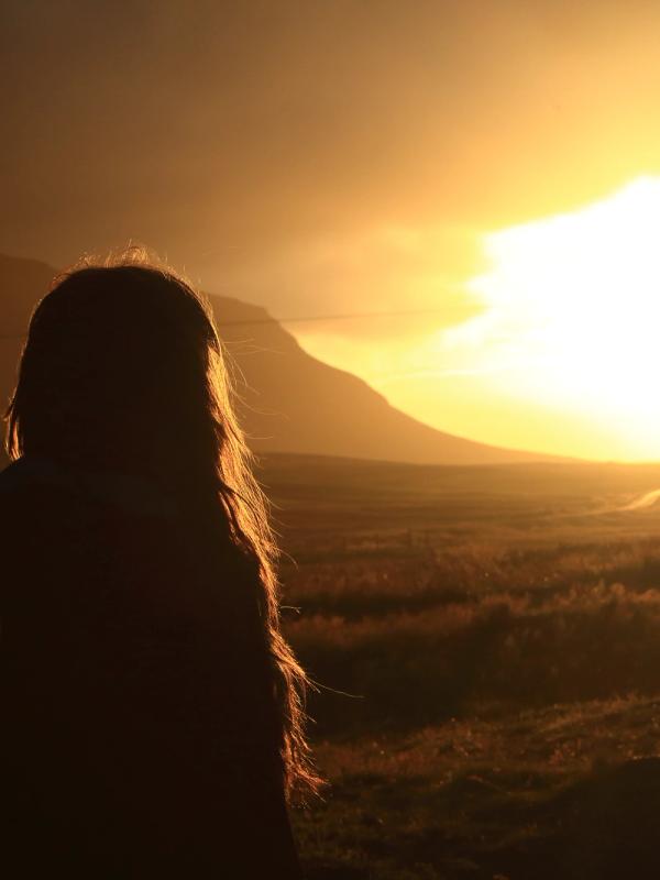 La silueta de una persona recortada contra un atardecer dorado sobre las montañas.