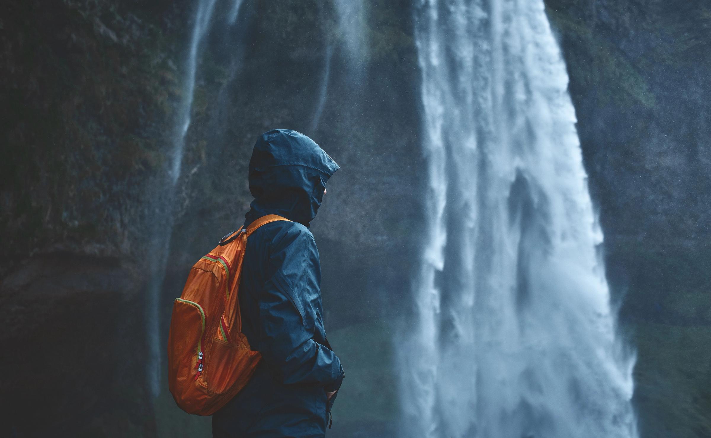 una persona con un chubasquero azul y una mochila naranja junto a una cascada