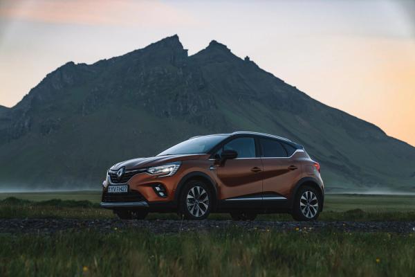 Bronze Renault Captur SUV parked on a gravel path with dark green mountains and a soft sunset sky in the background.