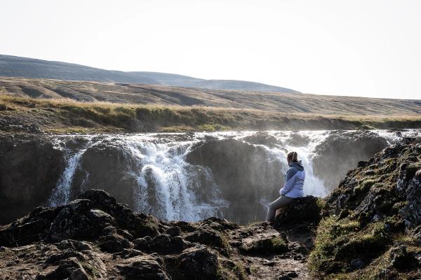 a woman is sitting on a rock near a waterfall .