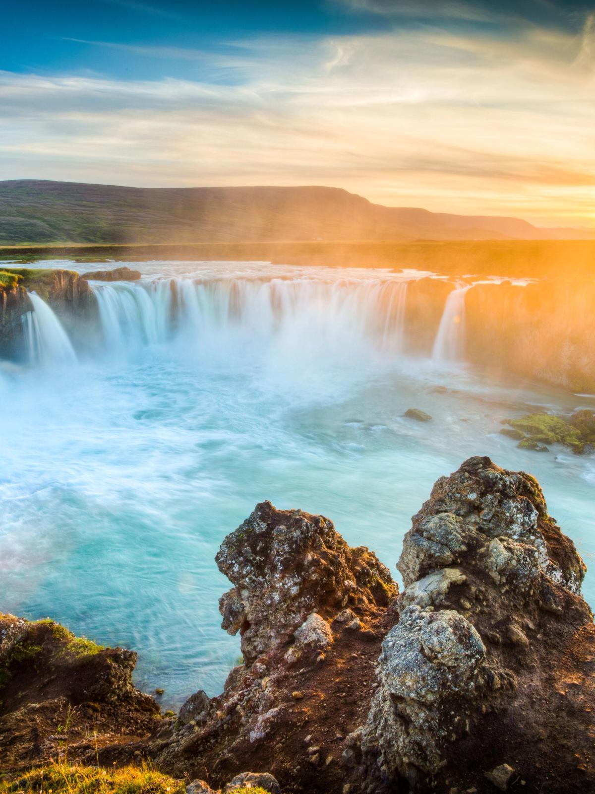 Panorámica de una cascada turquesa con el sol saliendo detrás de una montaña