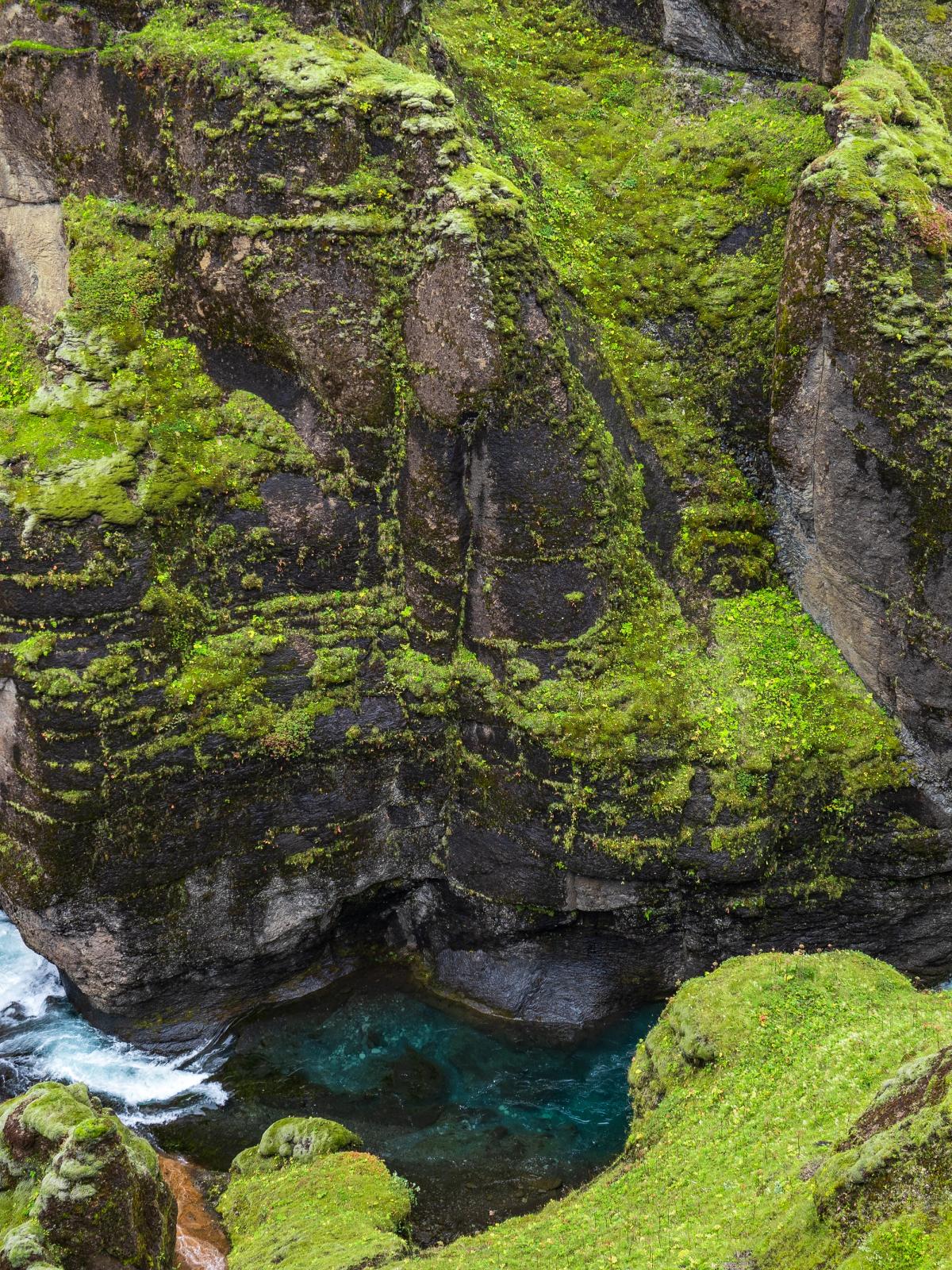 there is a waterfall in the middle of a canyon surrounded by mossy rocks .