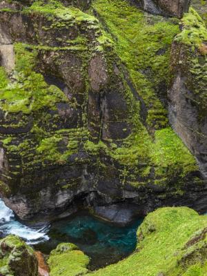 there is a waterfall in the middle of a canyon surrounded by mossy rocks .