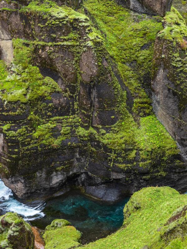 there is a waterfall in the middle of a canyon surrounded by mossy rocks .