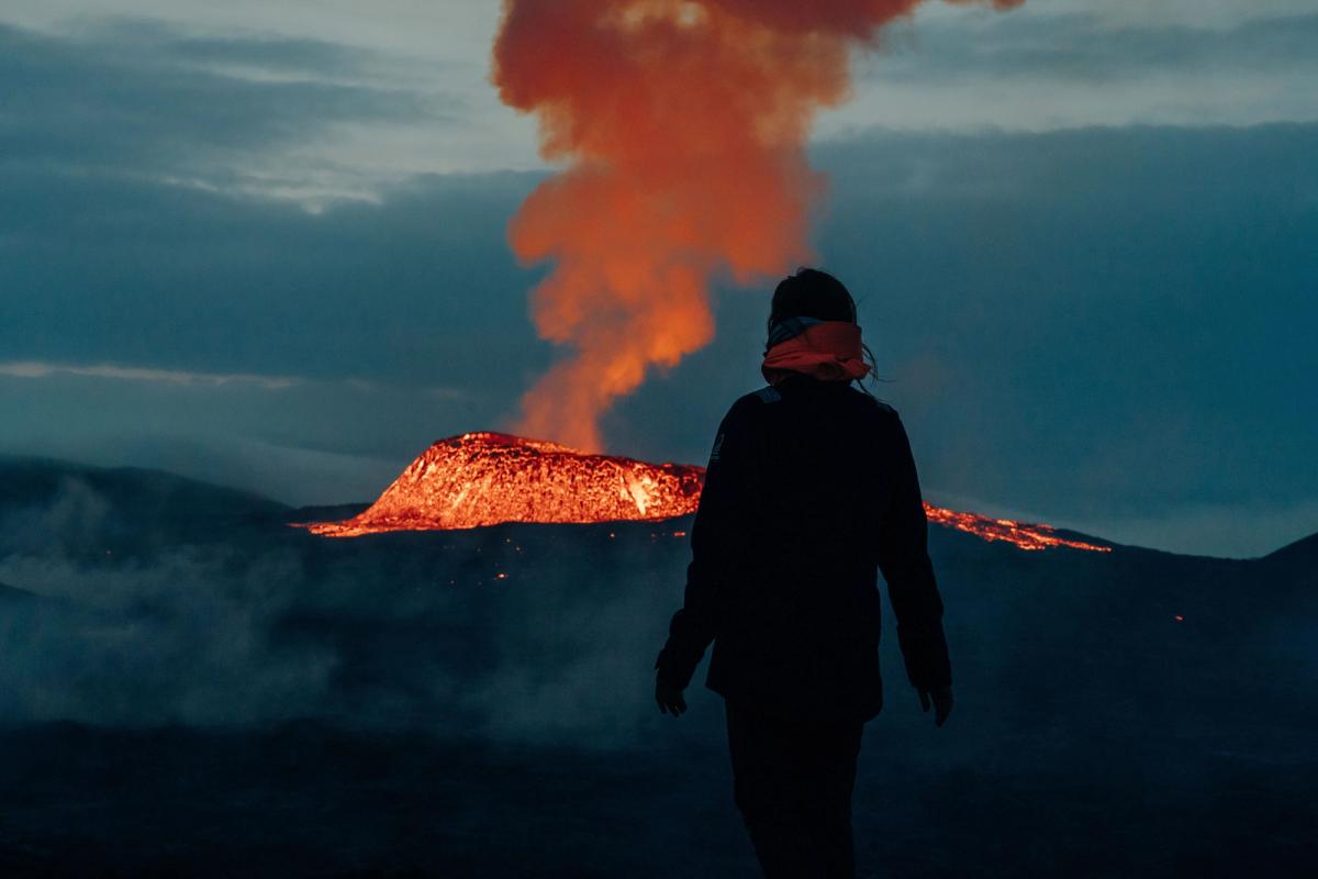 Persona admirando un volcano en erupción por la noche