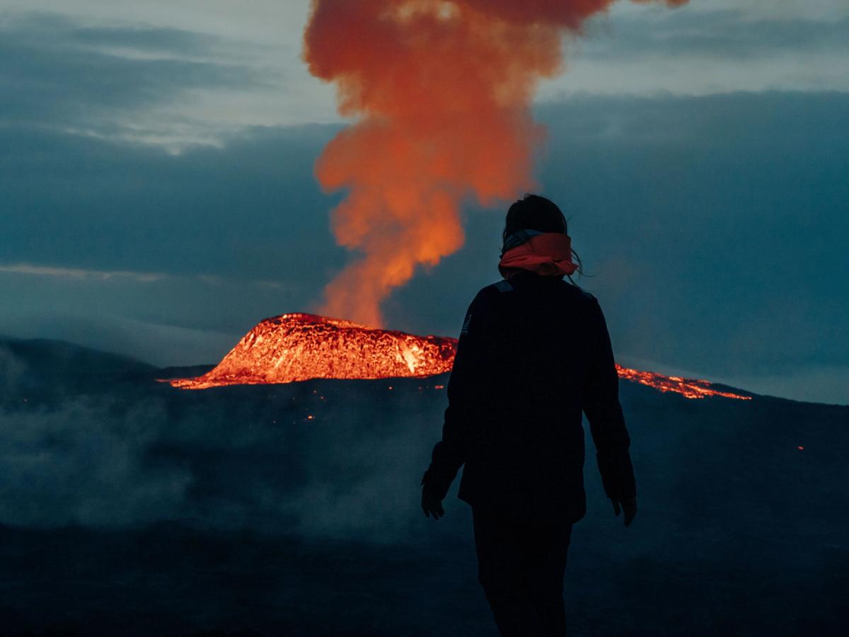 Persona admirando un volcano en erupción por la noche