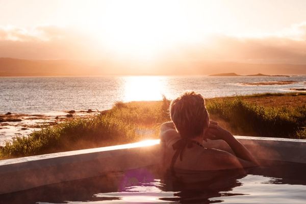 a woman is laying in a hot tub overlooking the ocean at sunset at sæberg in iceland.
