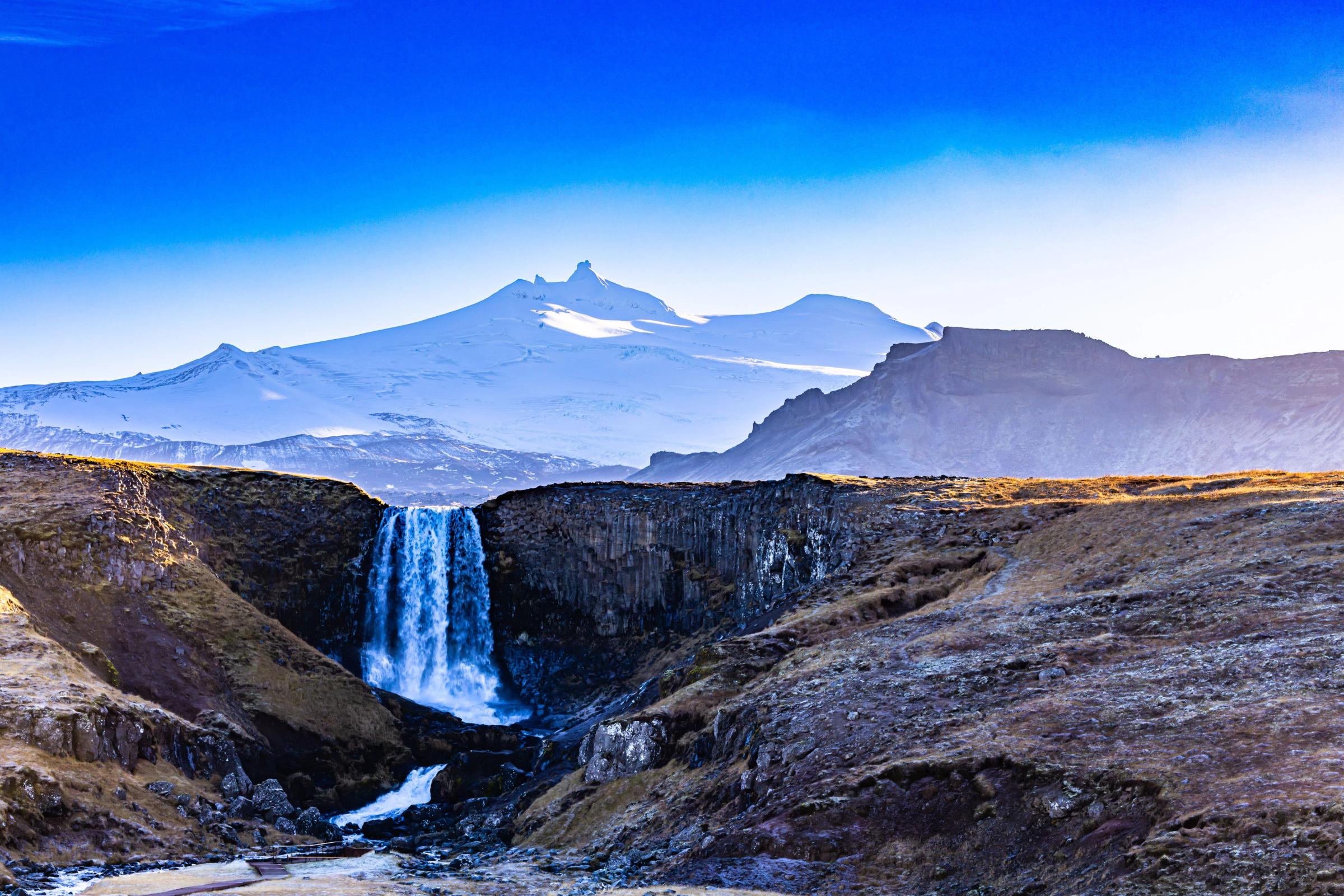 a waterfall in the middle of a canyon with mountains in the background .