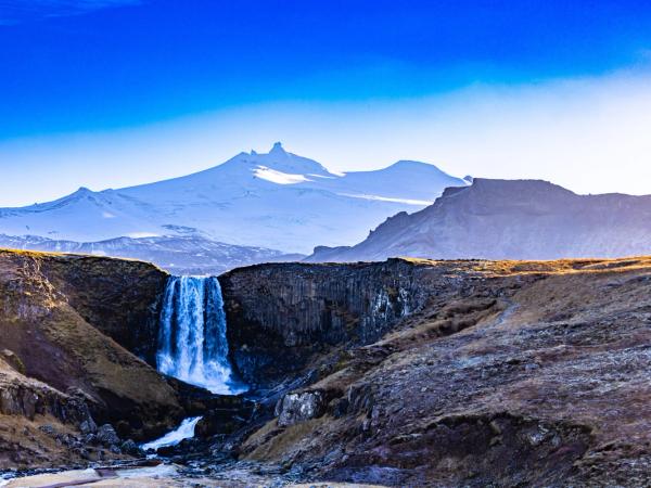 a waterfall in the middle of a canyon with mountains in the background .