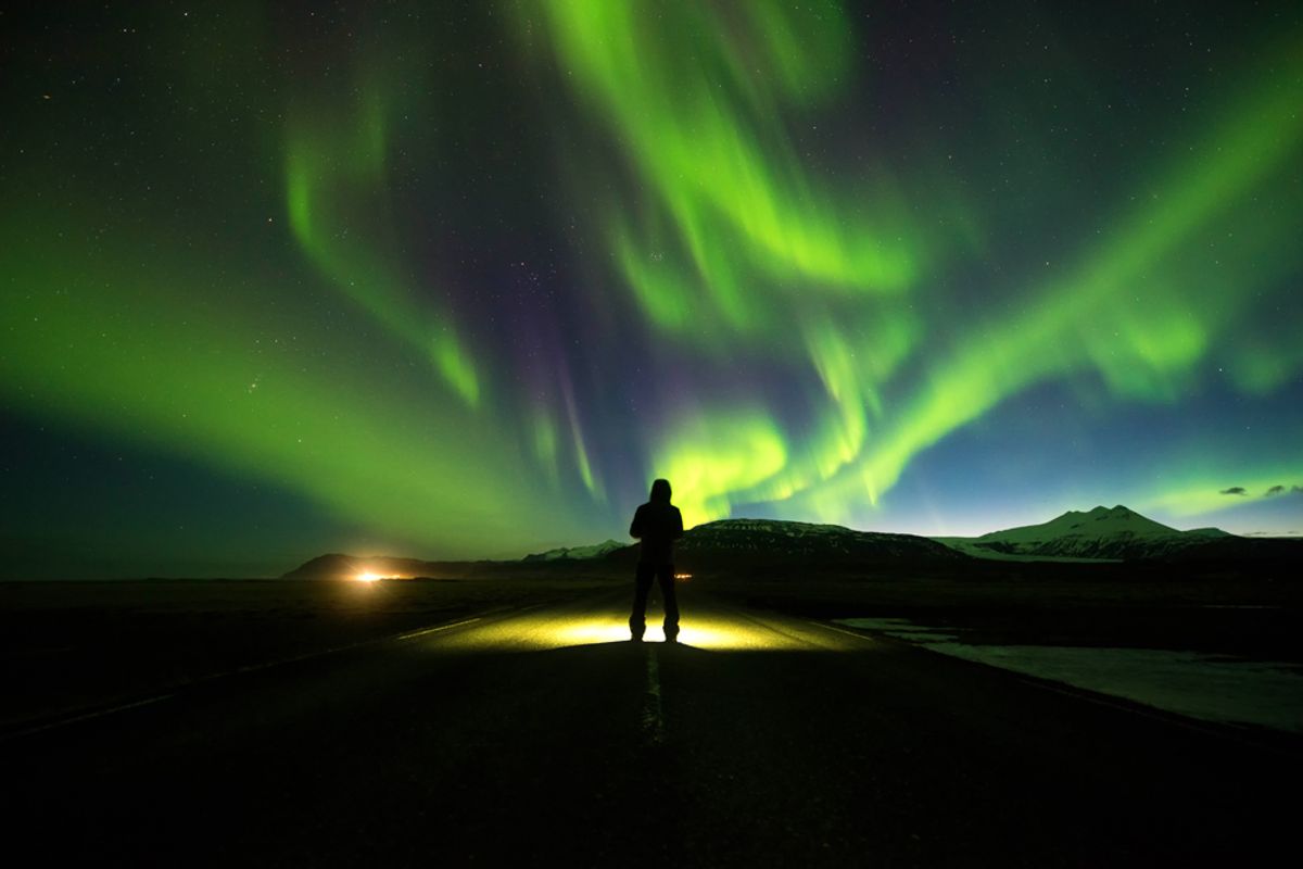 Una persona de pie sobre una carretera bajo la aurora boreal.